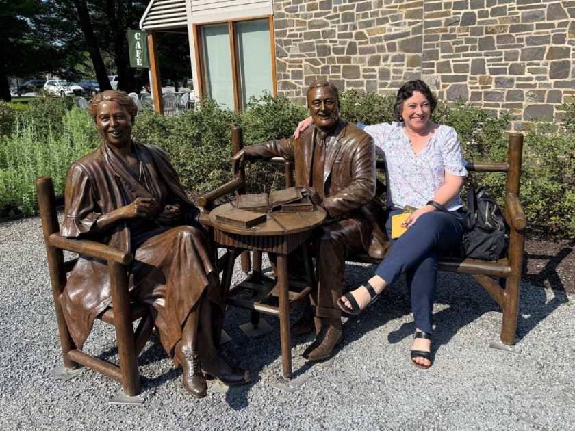 Julie sitting with statues of Franklin D Roosevelt and Eleanor Roosevelt in New York State