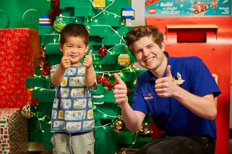 Master Model Builder Miller Keys with one of his assistants in front of the Christmas Bricktacular tree, giving a thumbs up